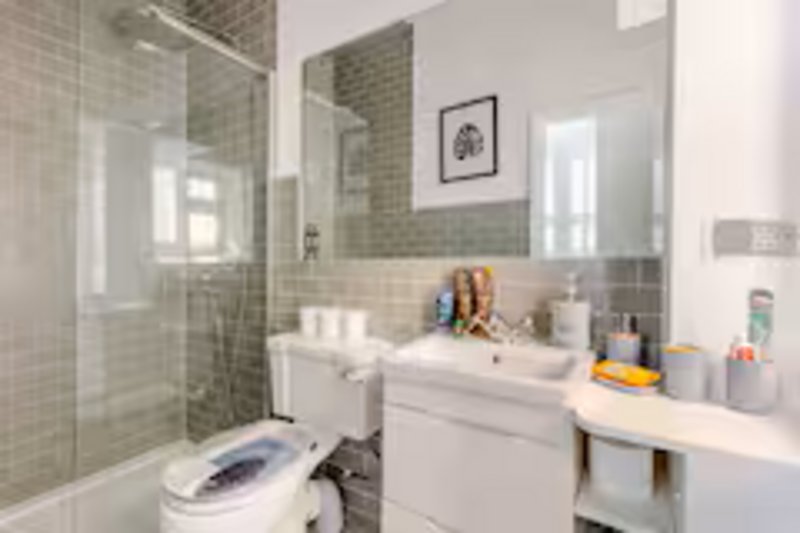 Modern bathroom with walk-in shower, white vanity, toilet and tiled walls