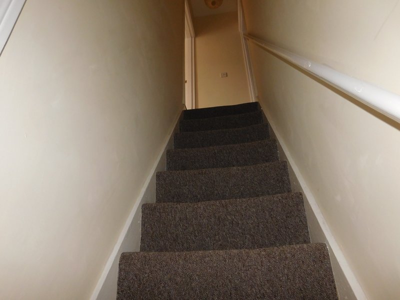 Narrow staircase with gray carpet treads and white walls leading upward
