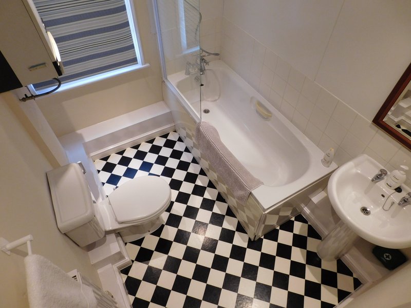Bathroom with black and white checkered floor, toilet, bathtub, sink and small window