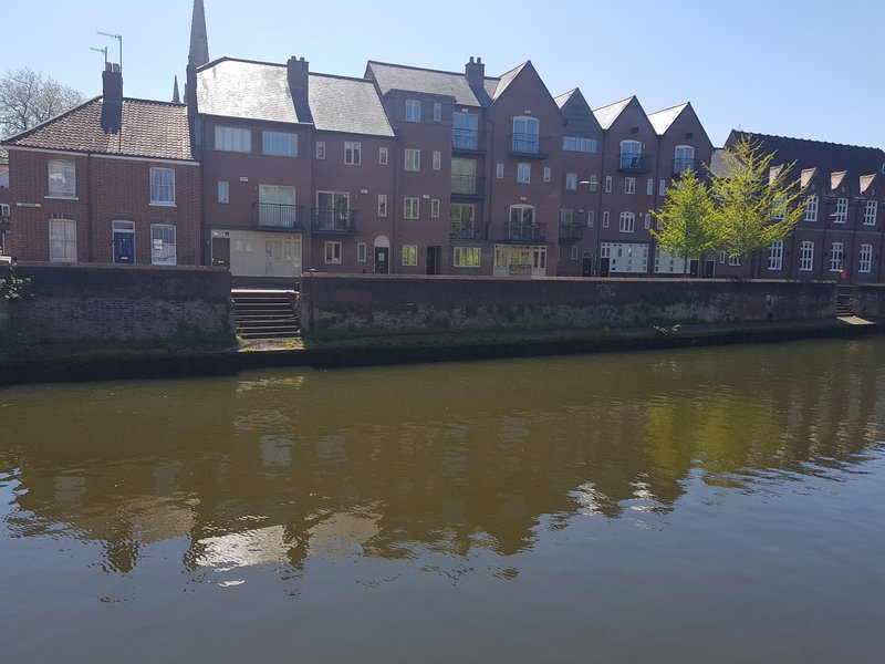 Row of brick townhouses along riverside with clear sky and water reflection