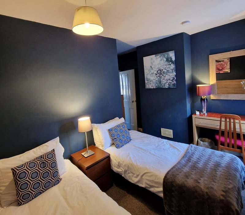 Twin bedroom with navy walls, bedside lamp, patterned cushions and desk area