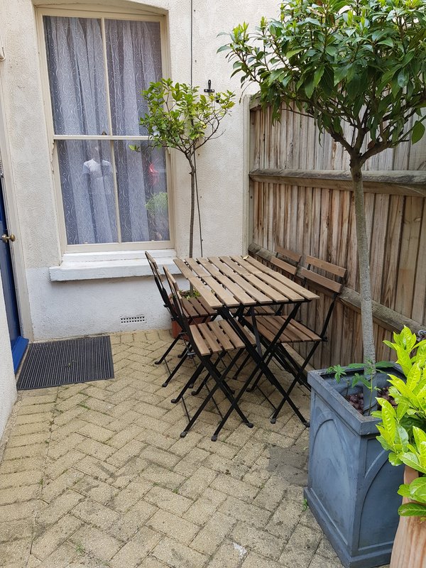 Small paved courtyard with folding table, chairs, potted plants and wooden fence