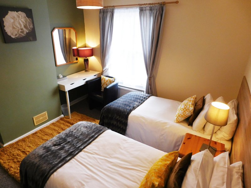 Twin bedroom with two single beds, desk, mirror, lamps and window with curtains