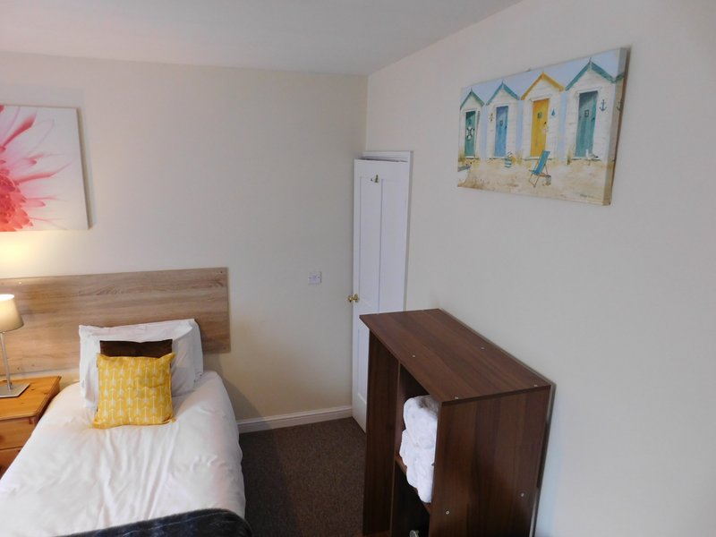 Bedroom with single bed, yellow cushion, wooden headboard, and dark wood furniture