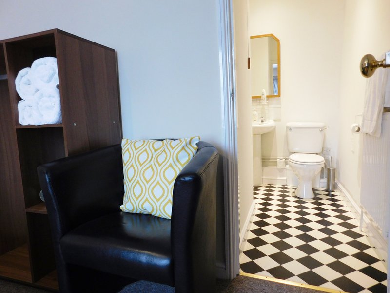 Bathroom with black and white checkered floor, toilet, sink, and adjoining room with armchair