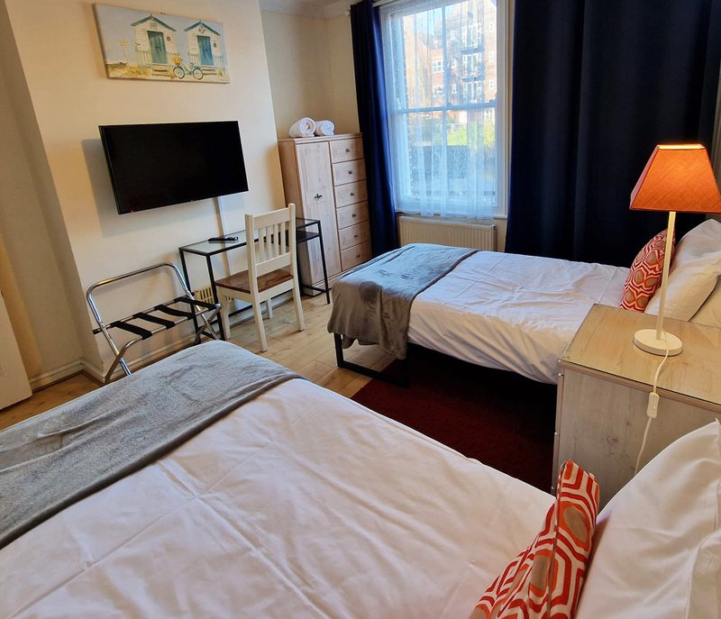 Bright bedroom with two beds, TV, desk area, window with city view and orange lamp