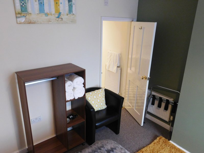 Small bedroom with dark wood shelf unit, black chair, wardrobe and cream-colored radiator