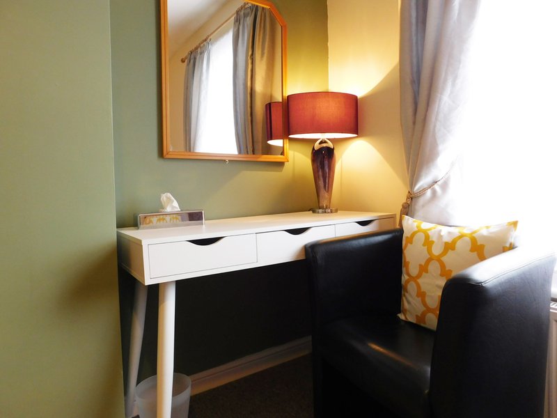 Bedroom desk area with mirror, lamp, yellow accent chair and white drawer unit