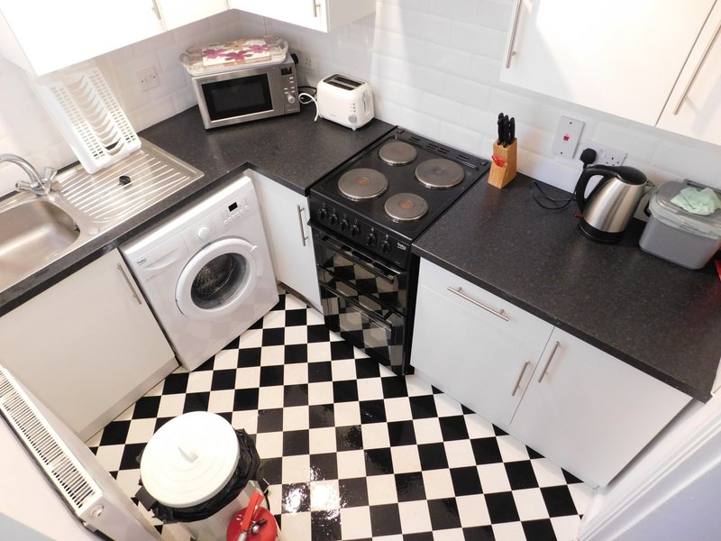 Compact kitchen with black and white checkered floor, white appliances, and dark countertop
