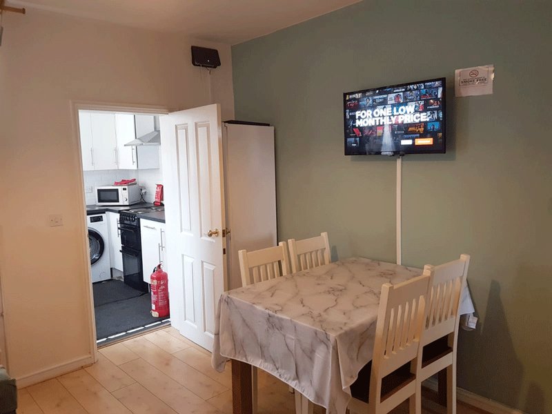 Dining area with wooden table, chairs, wall-mounted TV, and open doorway to kitchen