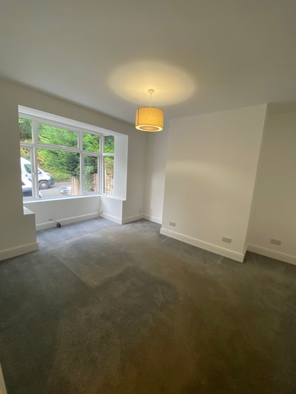 Empty living room with large windows, pendant light fixture, and gray carpeted floor
