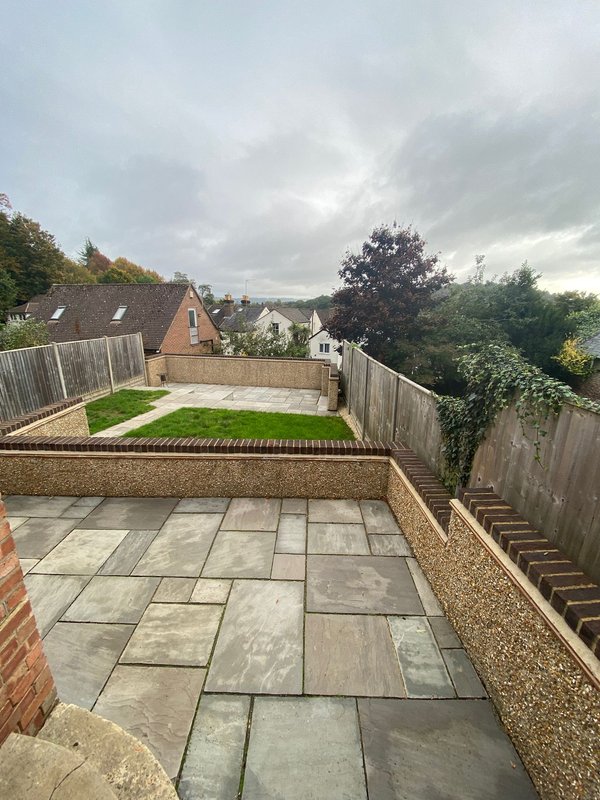 Rear garden with paved patio, lawn, wooden fencing, and brick house