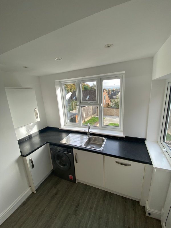 Modern kitchen with black countertop, white cabinetry, washing machine and garden view windows