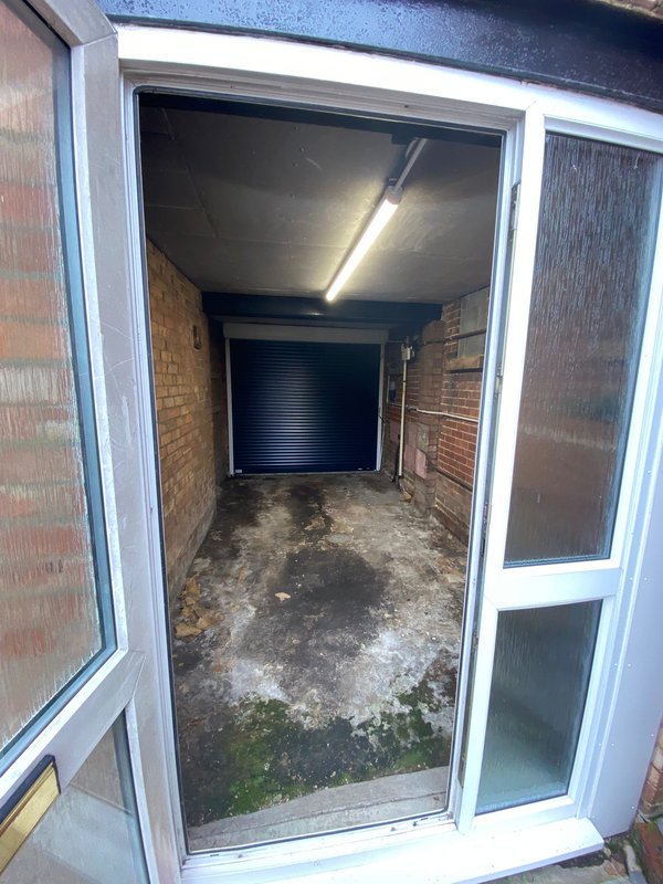 Brick garage interior with concrete floor, fluorescent lighting, and roller shutter door