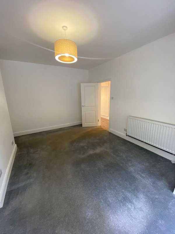 Empty bedroom with dark carpet, white walls, ceiling light fixture, radiator and open door