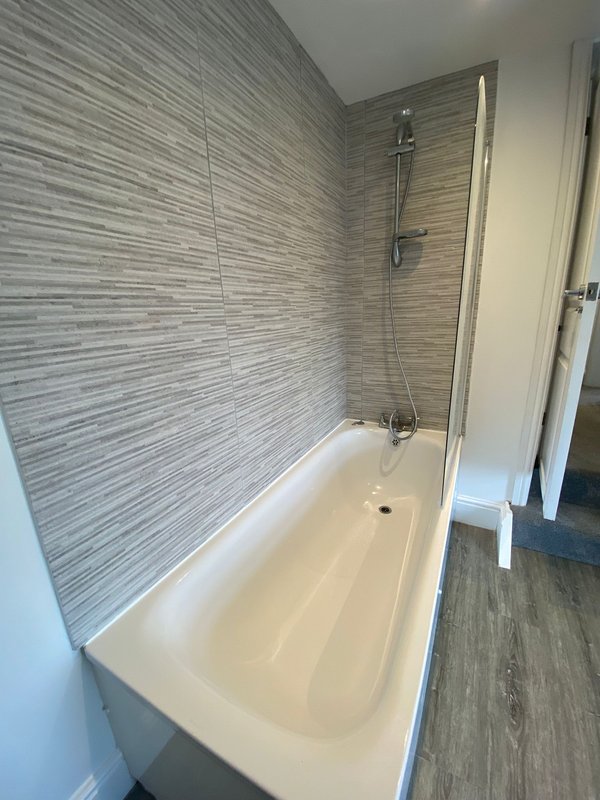 Modern bathroom with white bathtub, grey tile walls, and overhead shower