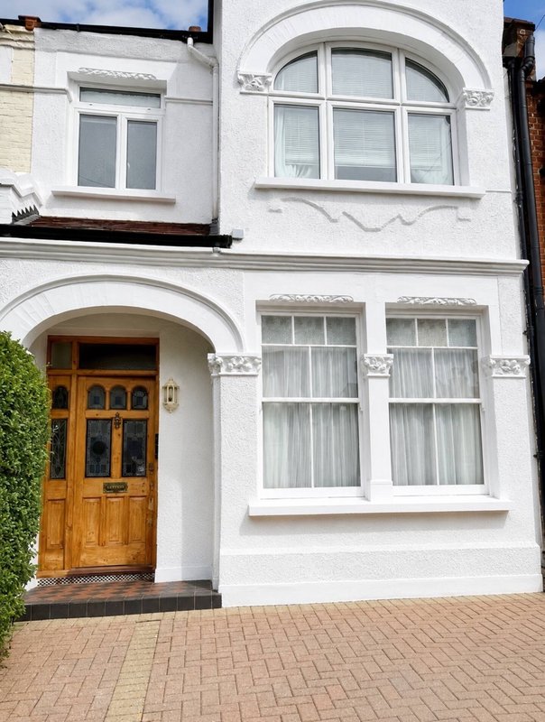 White-fronted residential building with wooden door, arched window and brick driveway