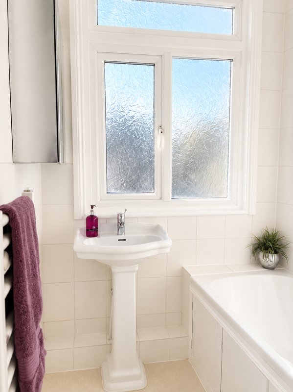 Clean white bathroom with pedestal sink, window, towel rail and bathtub