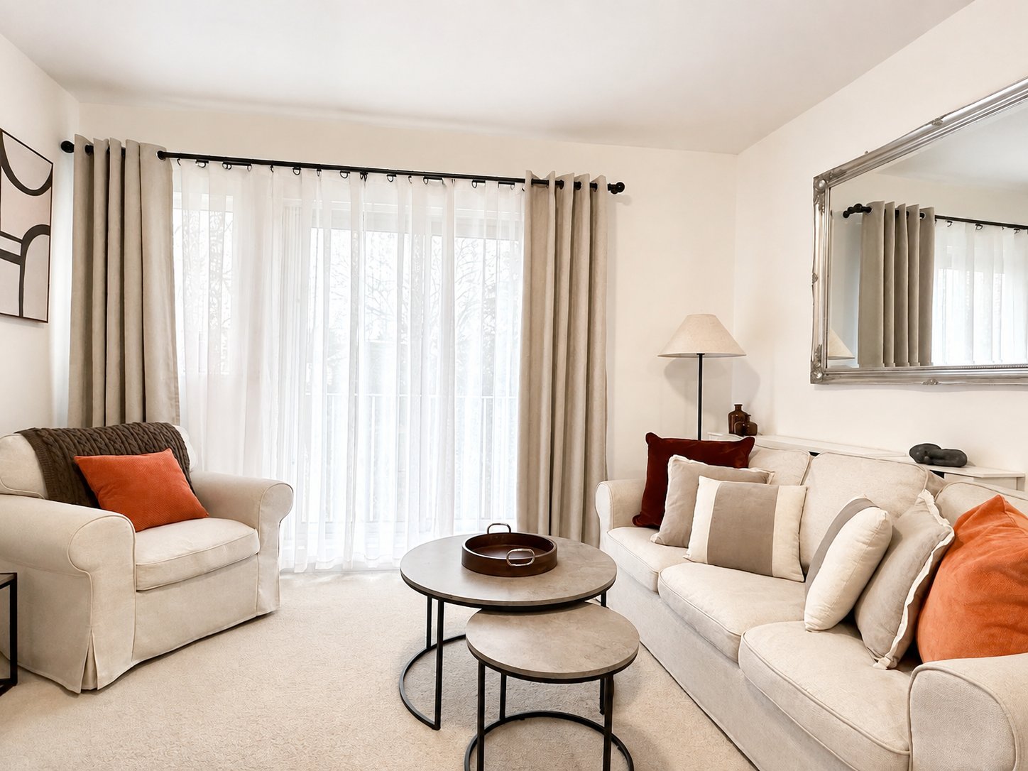 Bright living room with cream sofa, armchair, nesting tables and large windows with curtains