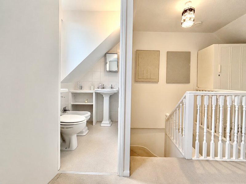 Attic bedroom with white crib, ensuite bathroom with toilet and pedestal sink
