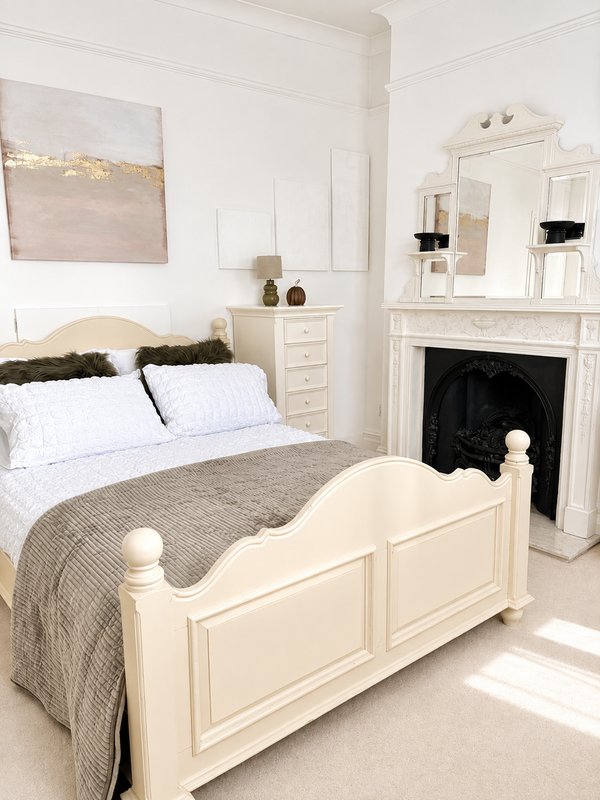 Bright bedroom with cream metal bed frame, white bedding, grey throw, fireplace and mirror