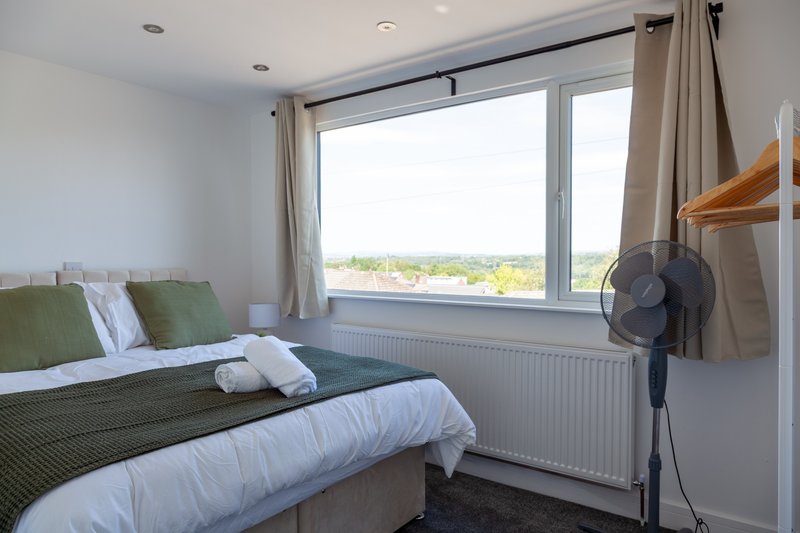Bright bedroom with double bed, large window, green bedding, and floor fan