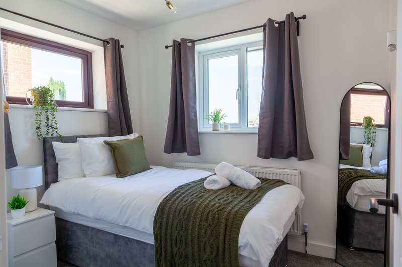 Bright bedroom with double bed, white bedding, olive throw, dark curtains and mirror