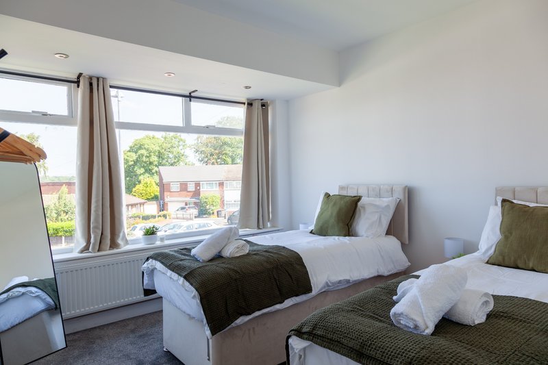 Bright twin bedroom with two beds, pillows, green throws, large windows with garden view