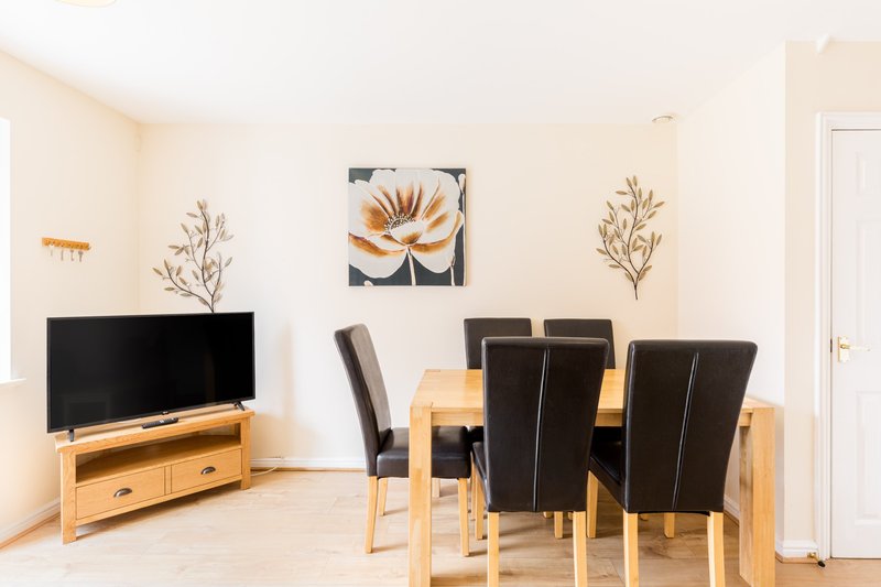 Open-plan living and dining area with TV, wooden furniture, and wall art