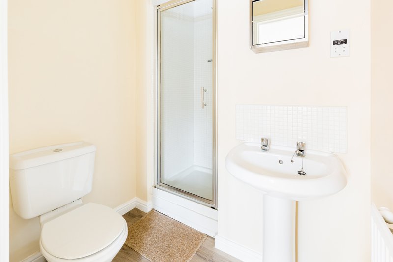 Clean bathroom with toilet, pedestal sink, shower enclosure and small window
