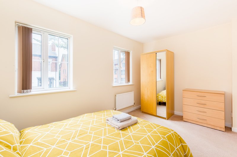 Bright bedroom with double bed, yellow geometric bedding, wooden wardrobe and chest of drawers