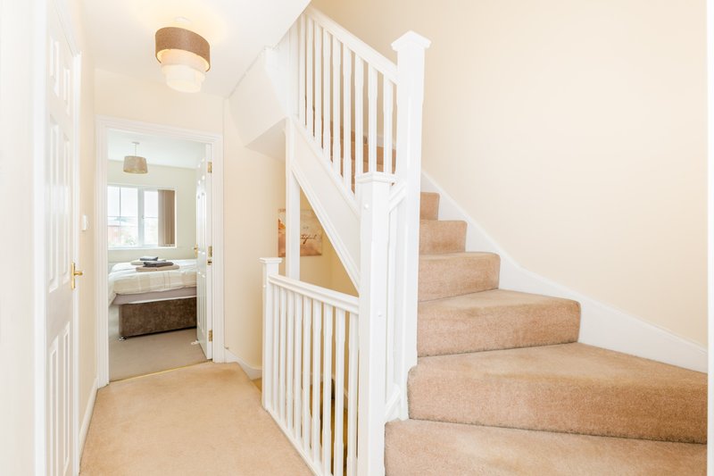 Bright hallway with carpeted stairs, white bannister and door to bedroom