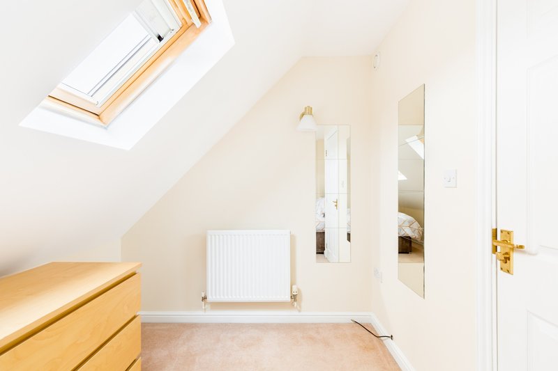 Bright attic bedroom with sloped ceiling, skylight, wooden furniture and radiator