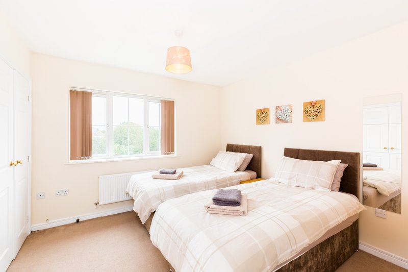 Bright twin bedroom with two single beds, wooden frames, beige bedding, large window and wall mirror