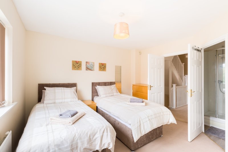 Bright twin bedroom with two single beds, wooden furniture, and ensuite bathroom visible