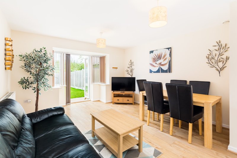 Open-plan living and dining room with black leather sofa, wooden dining table, garden view