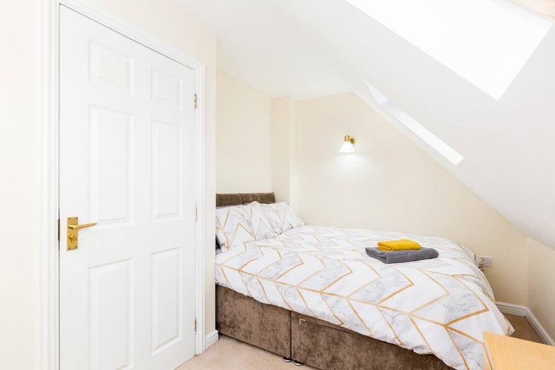 Bright attic bedroom with single bed, white door, skylight and wall lamp