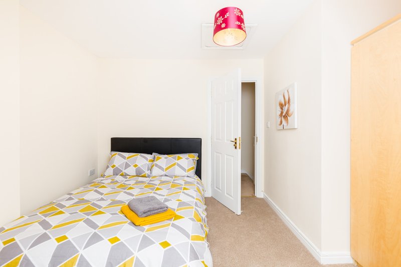Small bedroom with single bed, geometric patterned duvet, pink ceiling light and white wardrobe