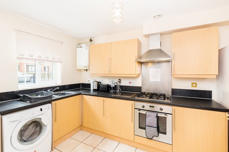 Modern kitchen with light wood cabinets, black countertops, built-in appliances and white tile flooring