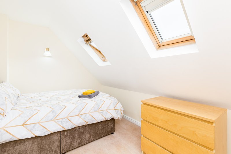 Bright attic bedroom with single bed, wooden dresser, and skylight windows
