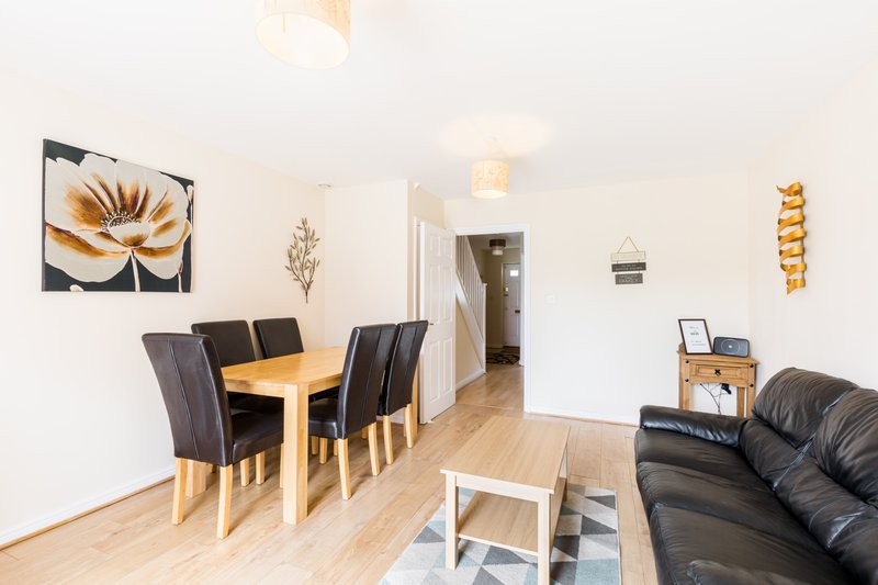 Open-plan living and dining area with wooden table, black chairs, leather sofa and wood flooring