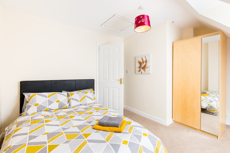 Bright bedroom with double bed, geometric yellow bedding, wooden wardrobe and red pendant lamp