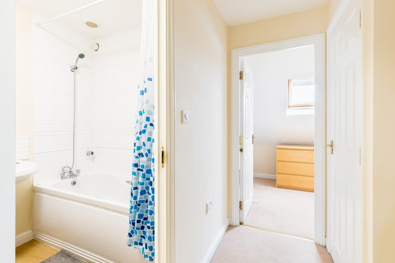 Bright bathroom with bathtub, blue tile shower screen, and doorway to bedroom