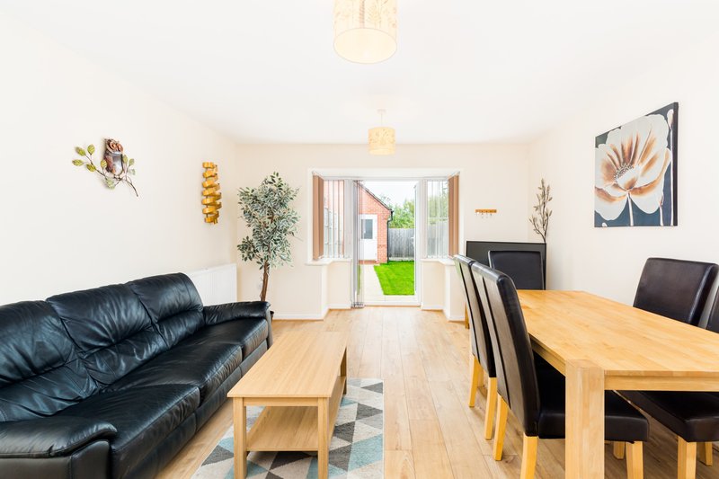 Open-plan living and dining area with black leather sofa, wooden dining table, and patio doors to garden