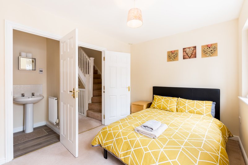 Bedroom with double bed, yellow patterned bedding, ensuite bathroom visible through open door