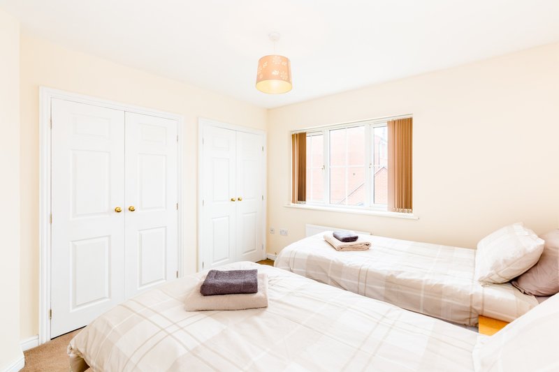 Bright bedroom with two single beds, white wardrobes, window with curtains and pendant light