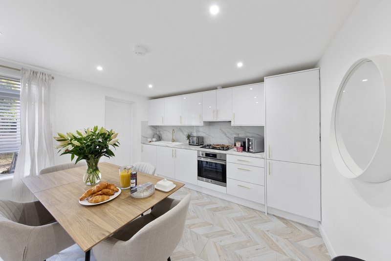 Modern white kitchen with wooden dining table, fresh flowers, and integrated appliances