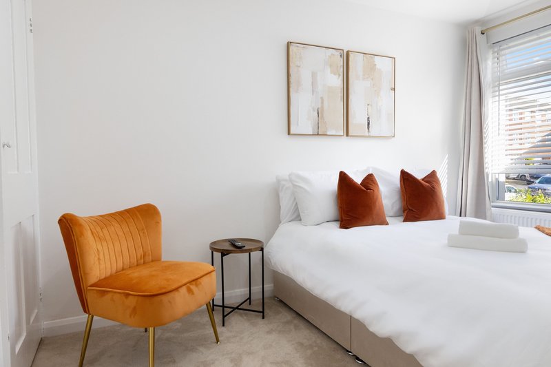 Bright bedroom with double bed, orange accent chair, side table and framed wall art