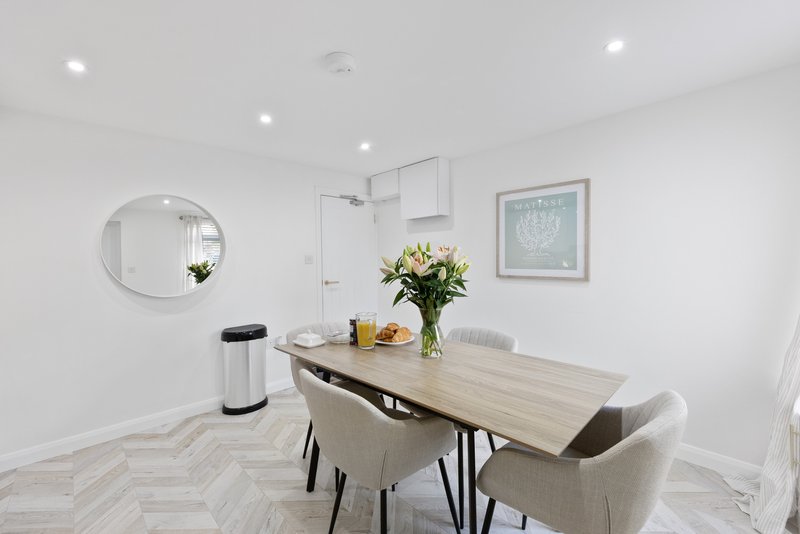 Modern dining area with wooden table, upholstered chairs, fresh flowers, and circular mirror