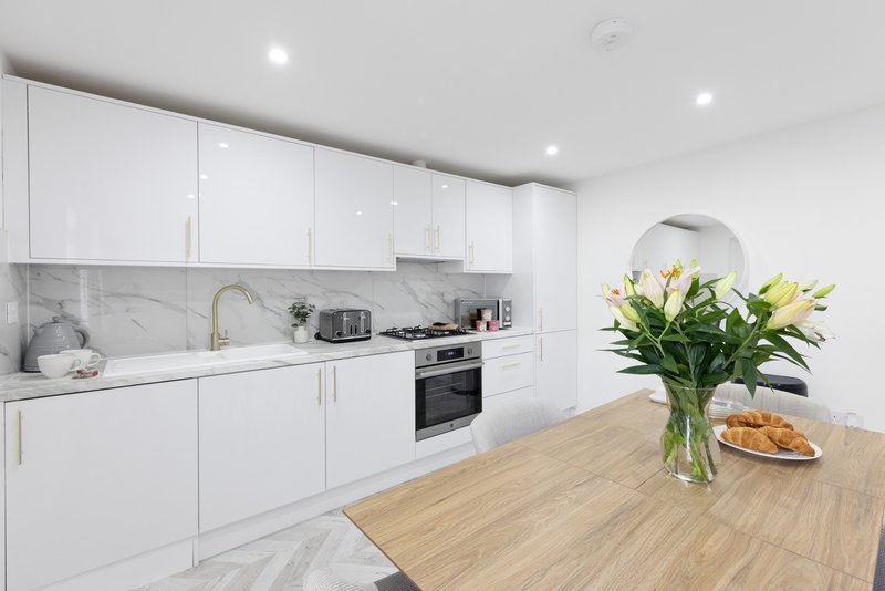 Modern white kitchen with marble backsplash, wooden island, and fresh flowers in vase